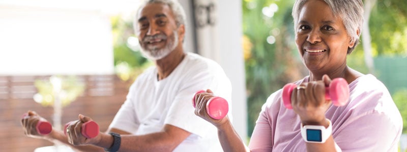 Older man and woman holding weights, exercising